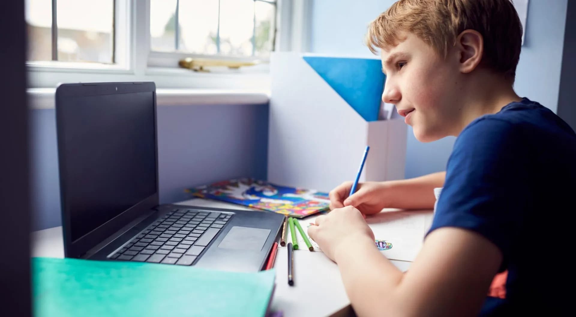 Middle school student writing at a desk beside a laptop