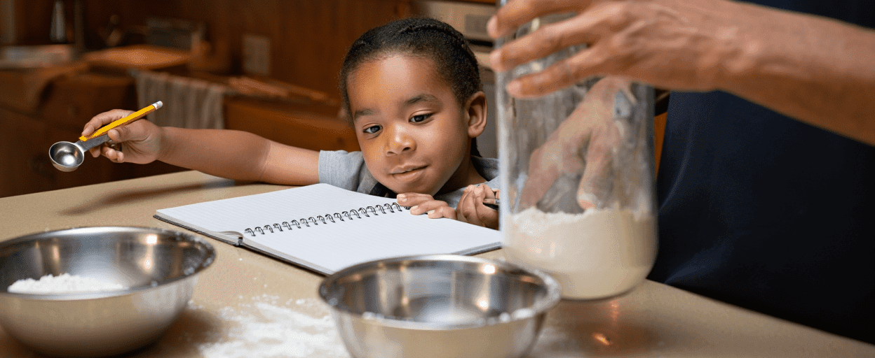 Child holding measuring spoon, adult's hand in flour jar, bowls of flour.